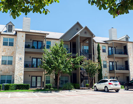 3-story limestone apartment buildings facing a parking lot